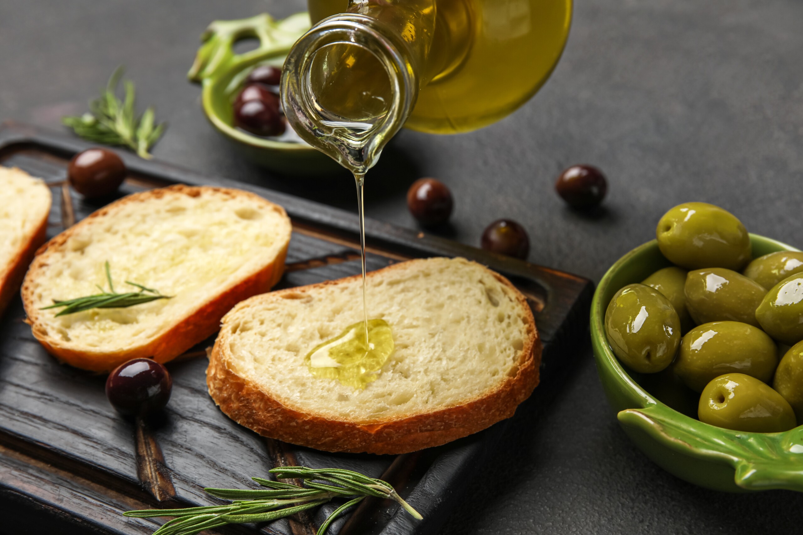 Pouring,Of,Olive,Oil,Onto,Fresh,Bread,On,Dark,Background,
